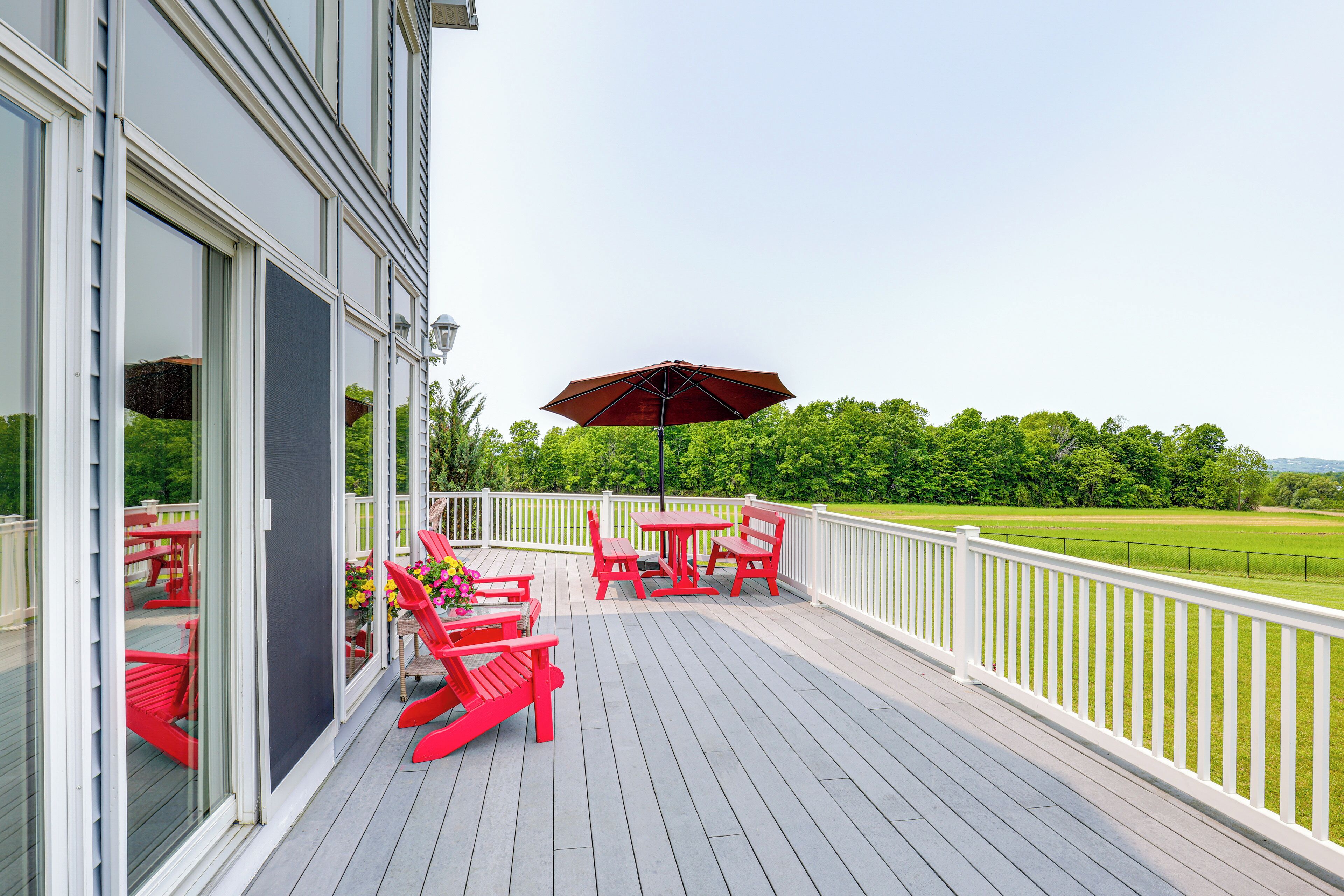 A deck with red chairs and a table, overlooking a green landscape.