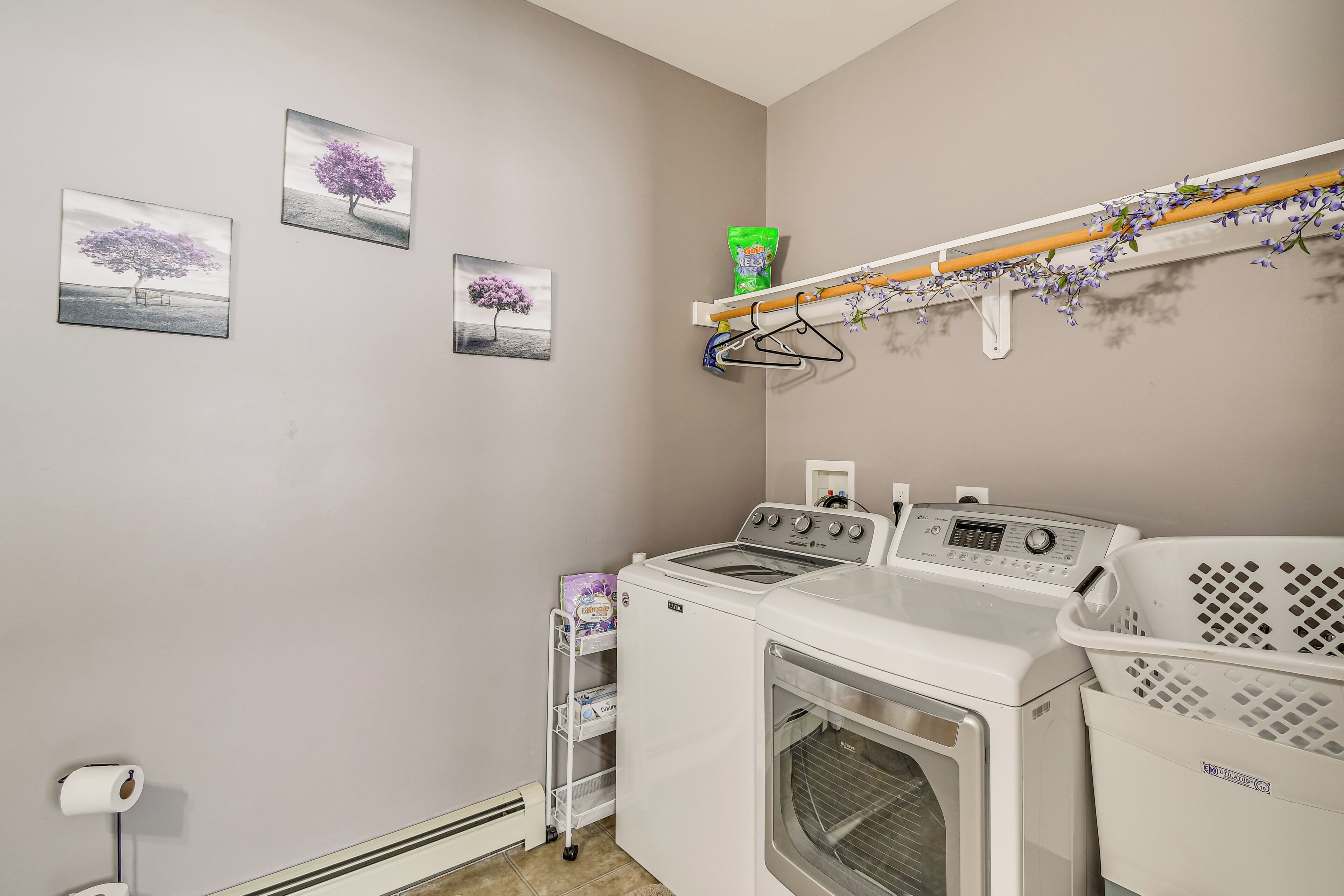 A laundry area with a washing machine, dryer, and a shelf with laundry baskets and a bag of detergent.