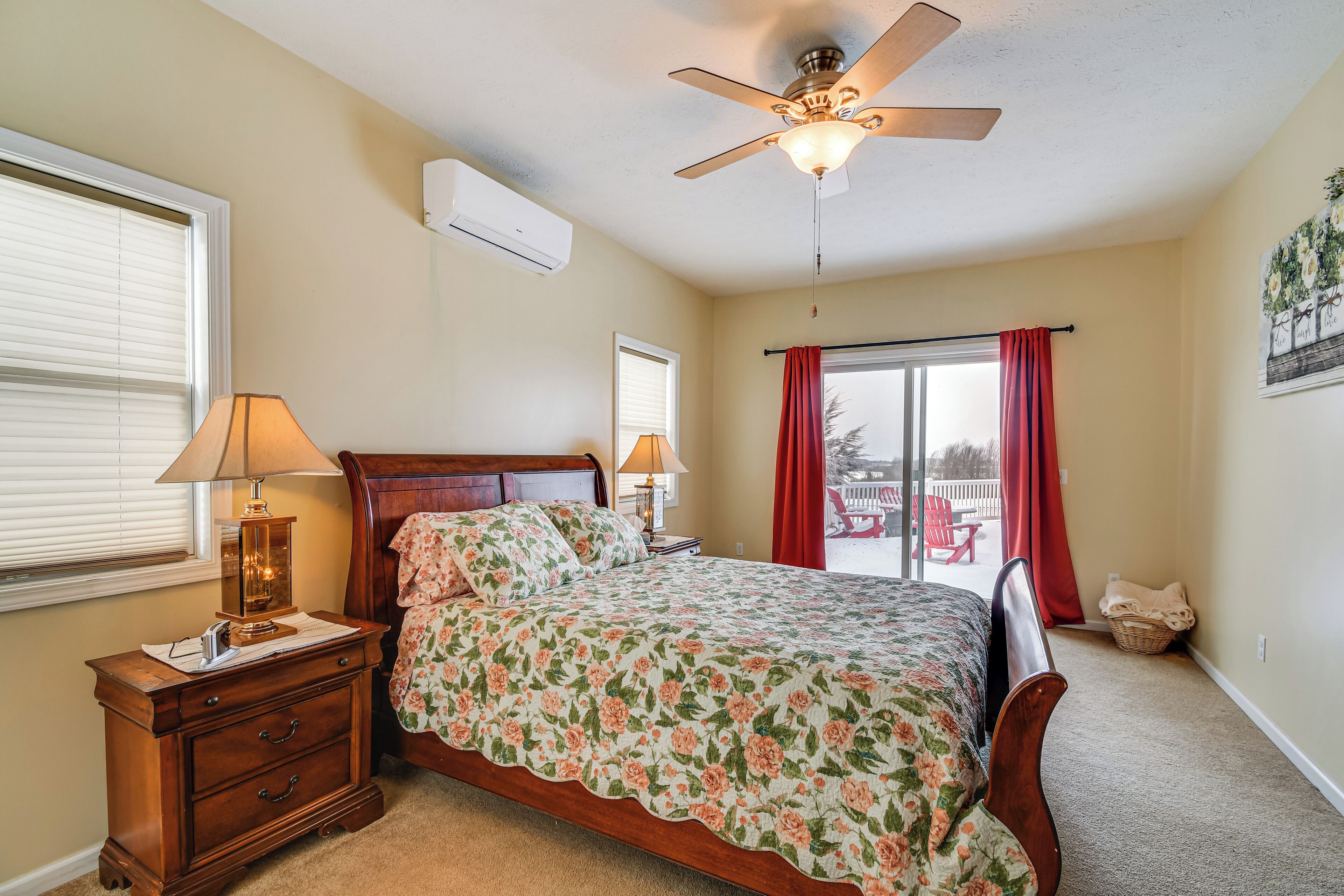A bedroom with a bed, a nightstand, a lamp, a ceiling fan, and a window with curtains.