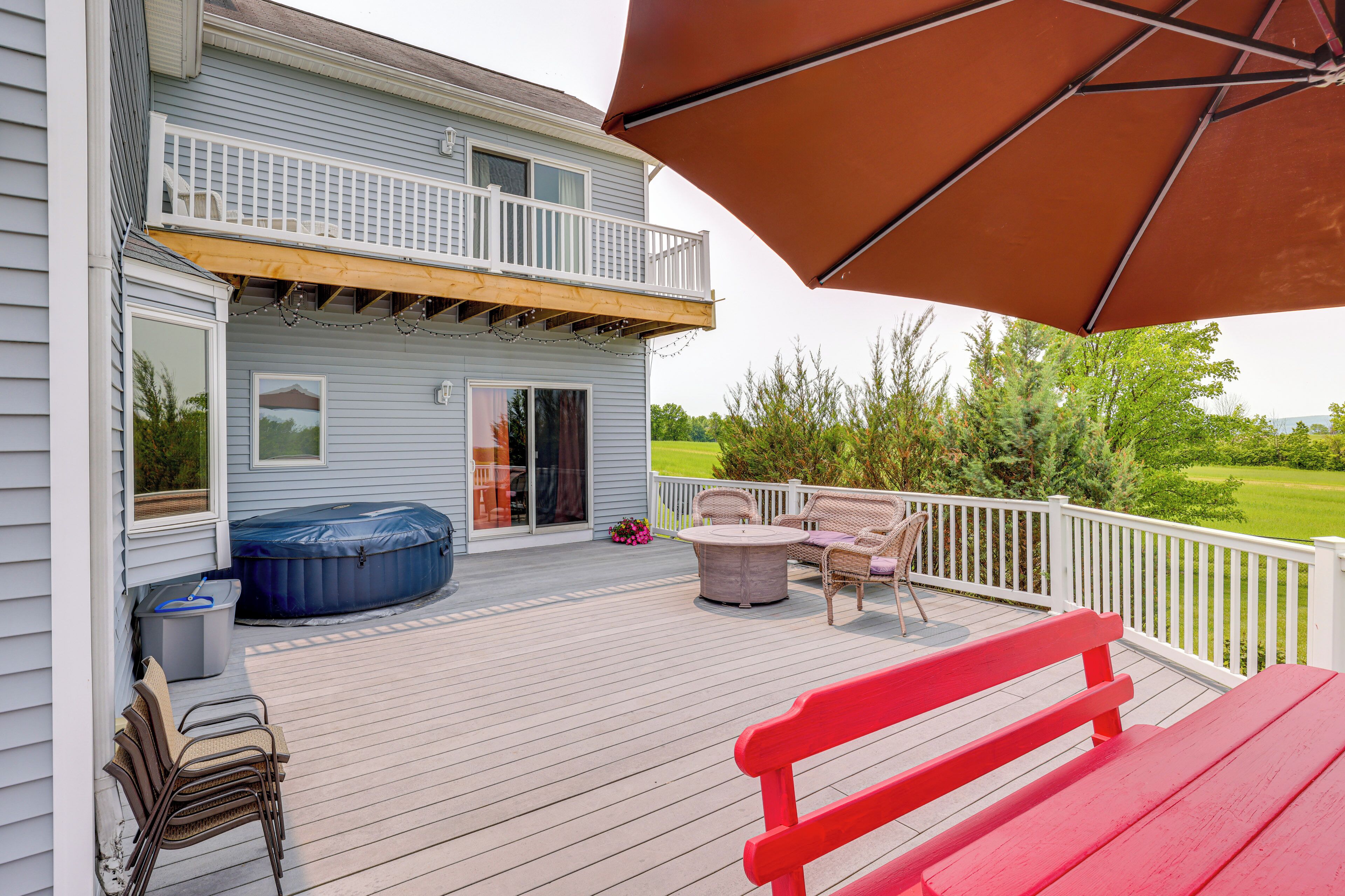 A deck with outdoor furniture, a hot tub, and a covered area with an umbrella.