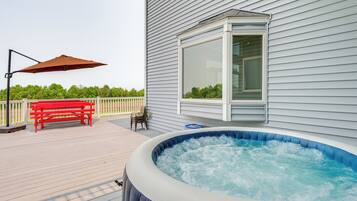 A hot tub on a wooden deck with a red bench and a patio umbrella.