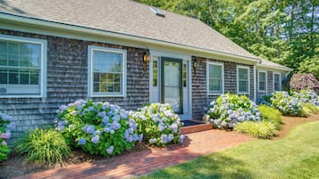 A residential house with a brick pathway, large windows, and a well-maintained garden with hydrangeas.