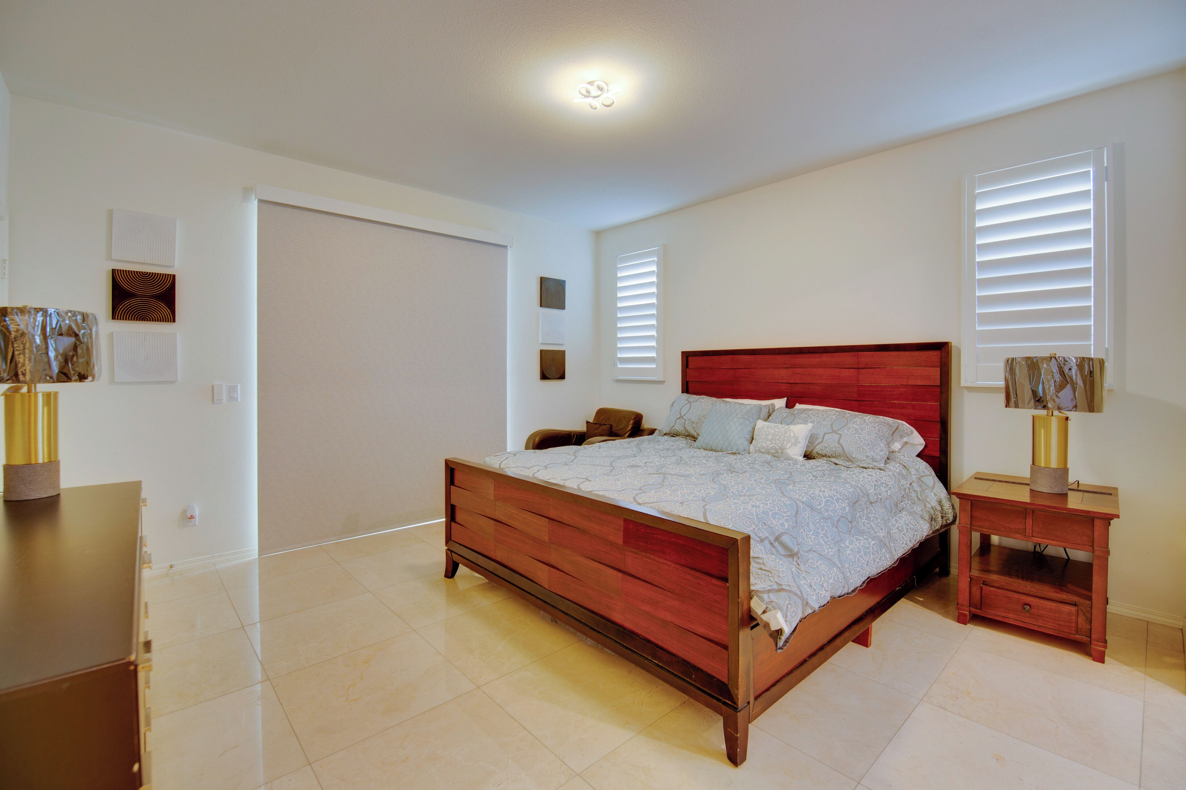 A bedroom with a wooden bed, a nightstand, a dresser, and a wall-mounted lamp.