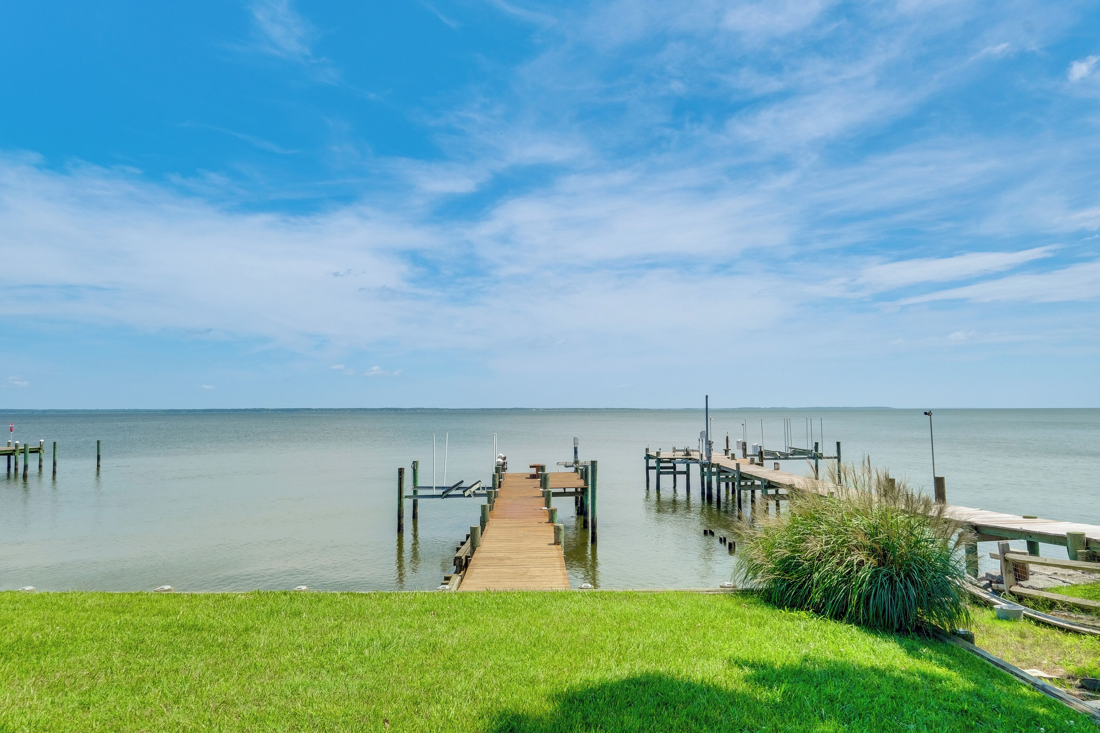 A wooden pier extending into calm water with a grassy area in the foreground.