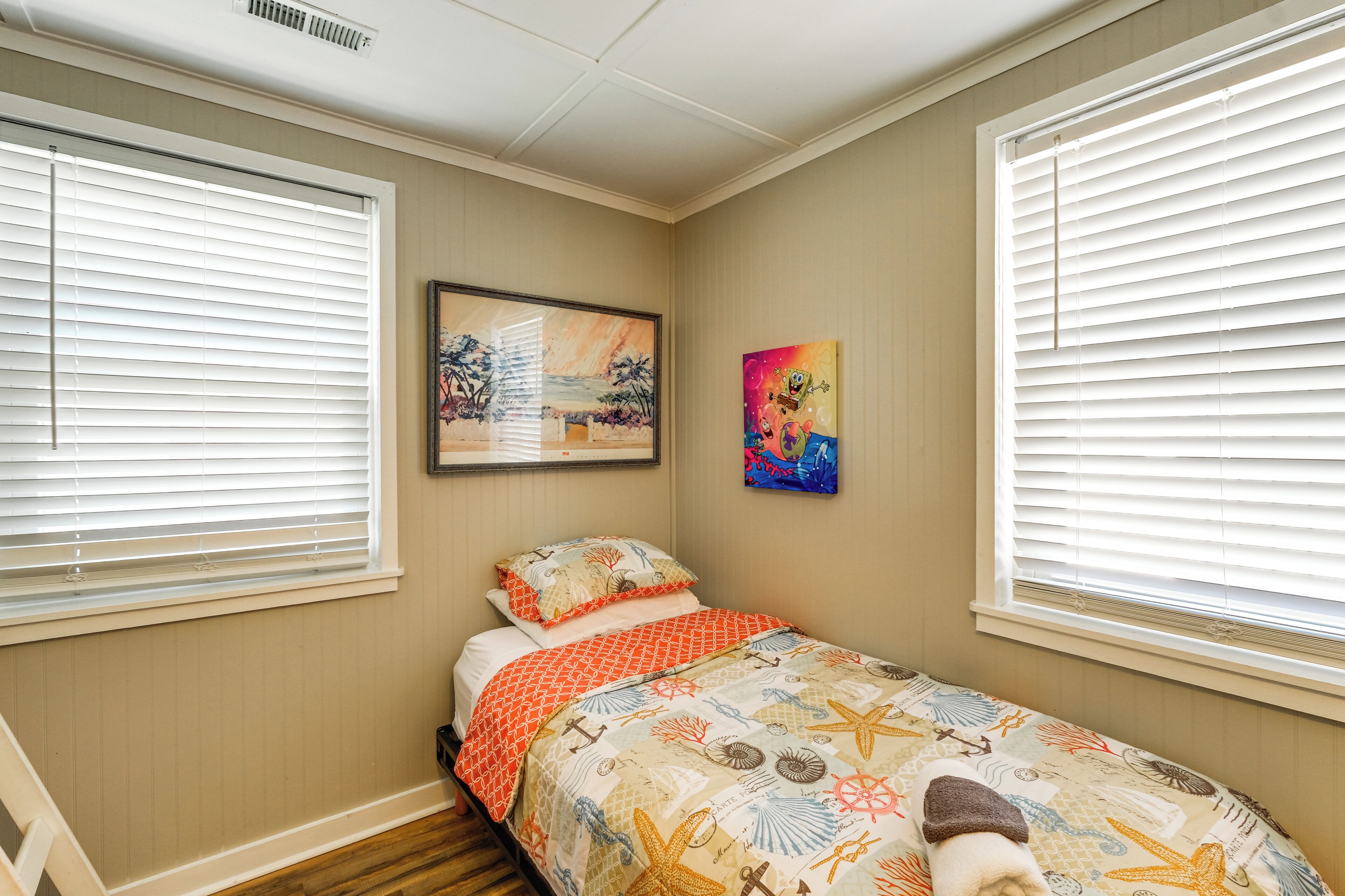 A bedroom with a bed, two windows with blinds, a painting on the wall, and a ceiling vent.