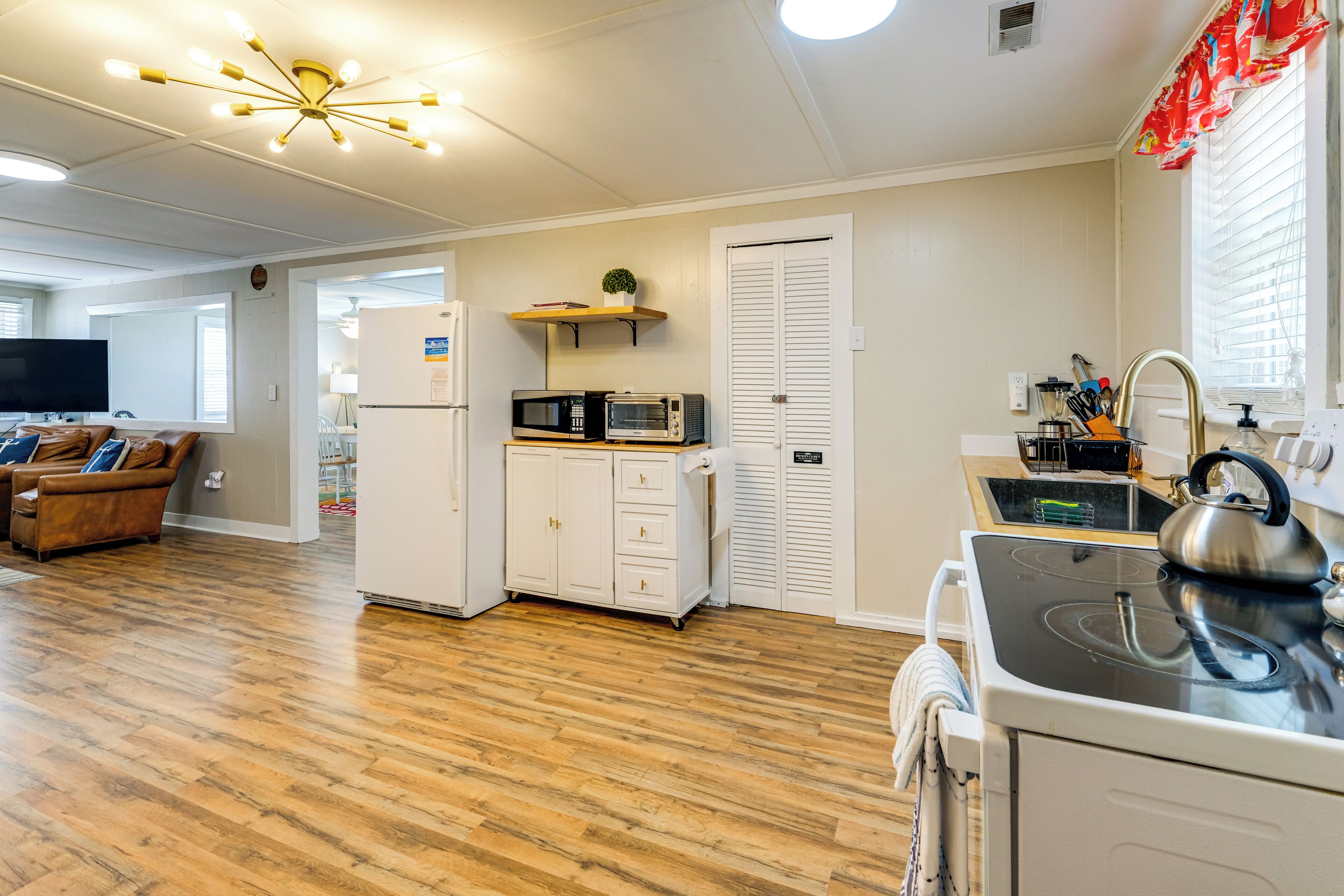 A modern kitchen with a stove, microwave, and refrigerator. There is a wooden floor and a ceiling light fixture.