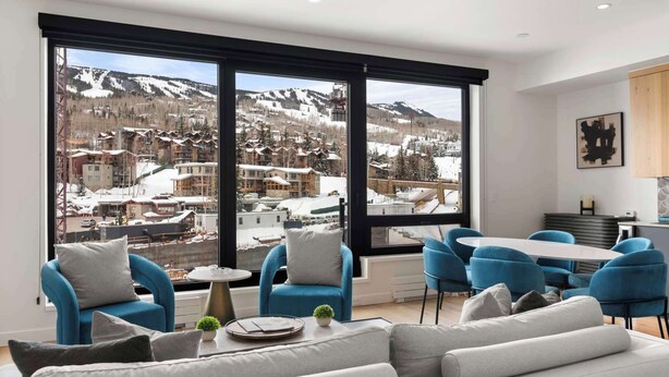 Een moderne woonkamer met een groot raam met uitzicht op een besneeuwde bergstad.