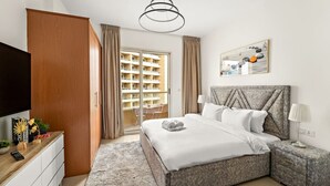 A modern hotel room with a large bed, a TV, a desk with a computer, and a view of the city through the window. - FIRST CLASS | Studio | Cozy & Chic Retreat (Dubai)