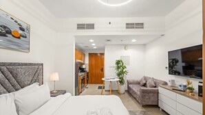 A modern hotel room with a large bed, a sofa, a TV, and a kitchenette. - FIRST CLASS | Studio | Cozy & Chic Retreat (Dubai)