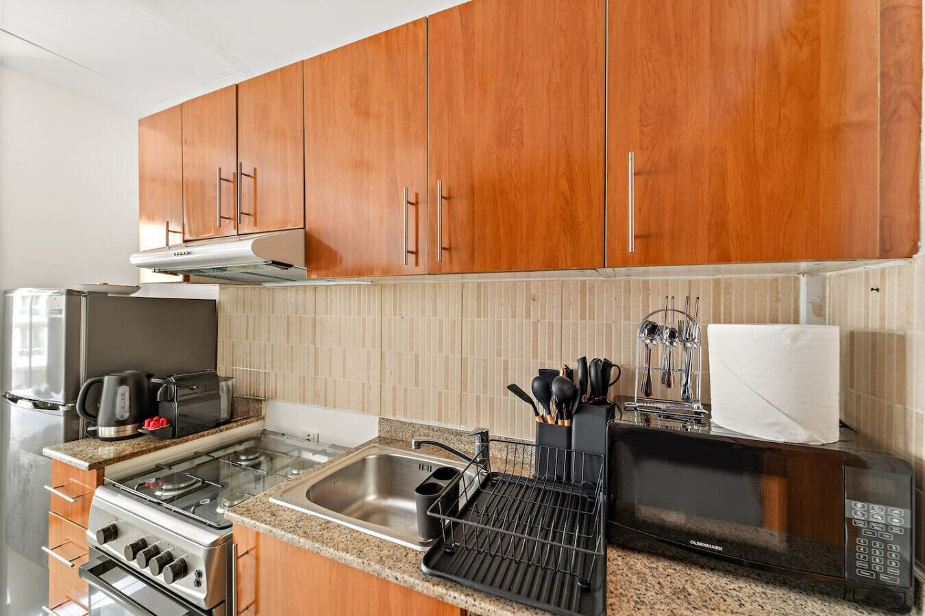 Een compacte keuken met houten kastjes, een roestvrijstalen spoelbak, een magnetron, een waterkoker en een kookplaat.