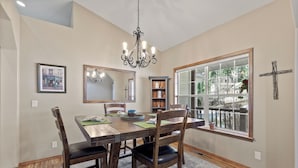 Un coin repas comprenant une table en bois, des chaises, un lustre, une grande fenêtre et un miroir.