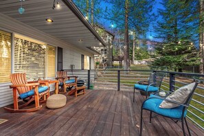 A wooden deck with outdoor seating, a covered porch, and a view of a forested area.