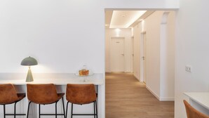 Un comedor moderno y minimalista con una mesa blanca, tres sillas marrones y una lámpara de mesa individual. Un expositor de vidrio con un postre se encuentra sobre la mesa.