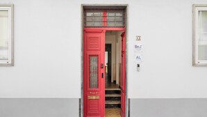 Una puerta roja con una reja de metal, un escalón pequeño que la precede, y un letrero que indica que la propiedad es un DAZ HOUSE.