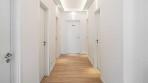 Un pasillo moderno y estrecho con paredes blancas y suelo de madera, que conduce a una puerta con el número 444.