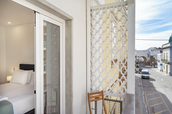 A hotel room with a bed, a chair, and a view of a street with buildings and a bridge. - Faro DAZ House by Get Your Stay (Faro)