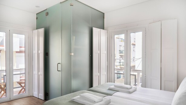 Habitación de hotel con cama, dos toallas, un armario verde y balcón con mesa y sillas.