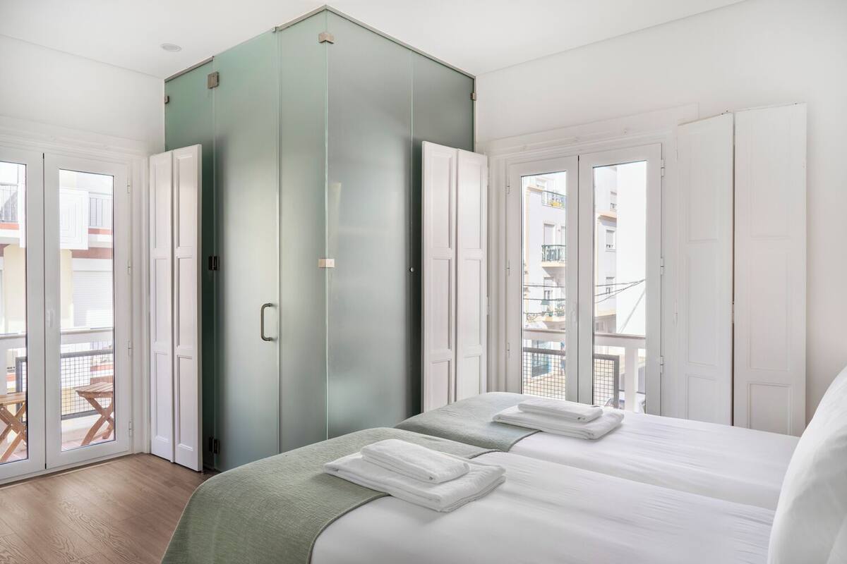A hotel room with a bed, two towels, a green cabinet, and a balcony with a table and chairs.