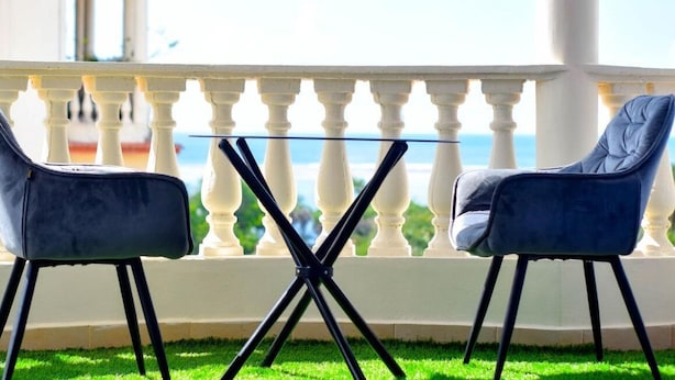 Two chairs and a table on a balcony with a white balustrade, overlooking a body of water.