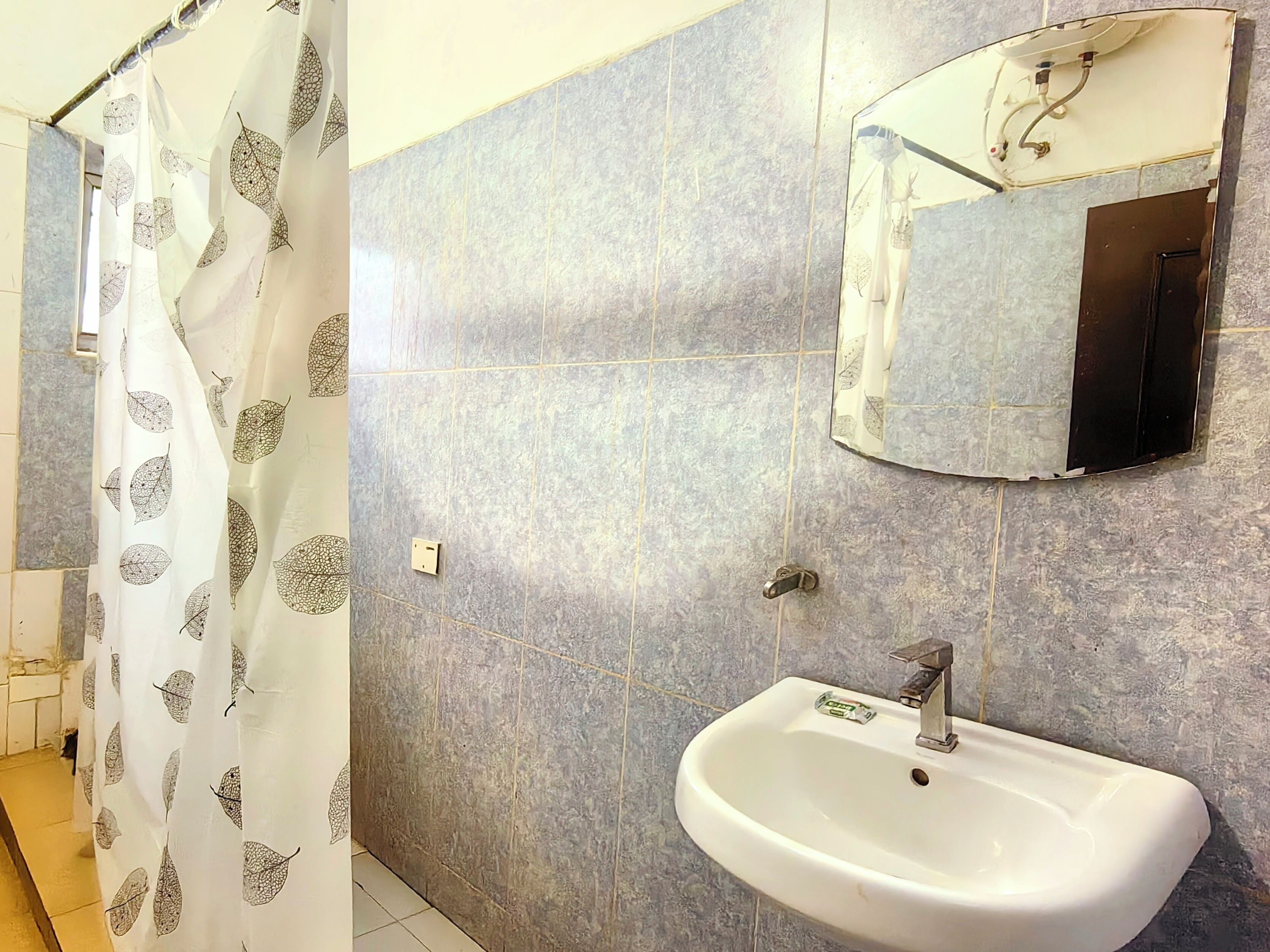 Un baño con un lavamanos blanco, un espejo y una cortina de ducha estampada con hojas.