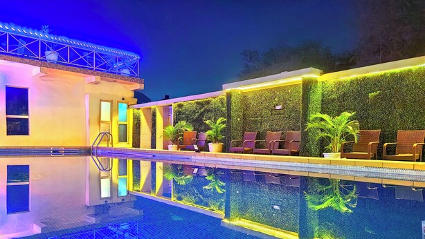 A swimming pool with a clear reflection, surrounded by a building with a green wall and seating area.
