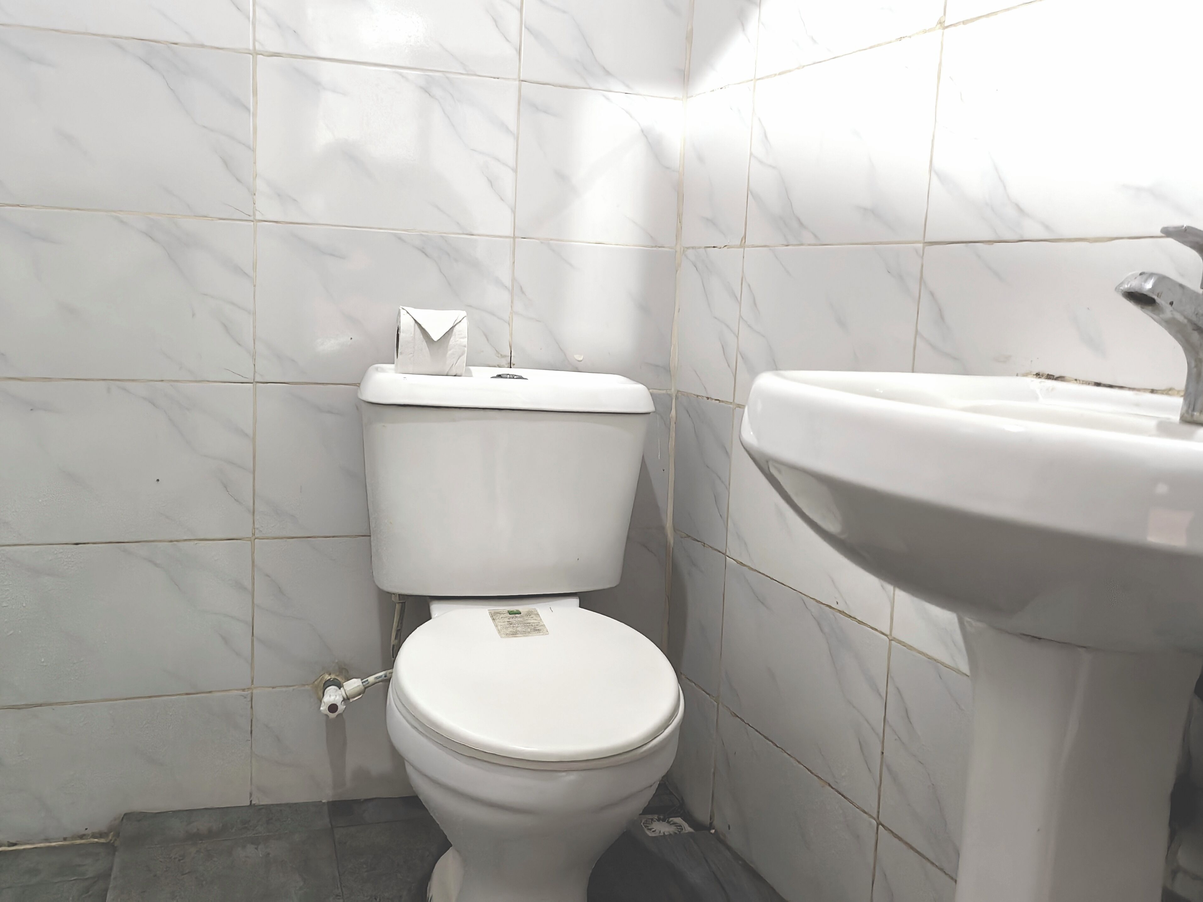 A bathroom with a toilet and sink, tiled walls, and a marble-like floor.