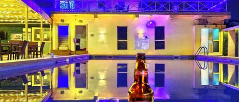 Zwembadgedeelte met een fles Budweiser en een glas, omringd door een gebouw met een balkon en een bord met zwembadregels.