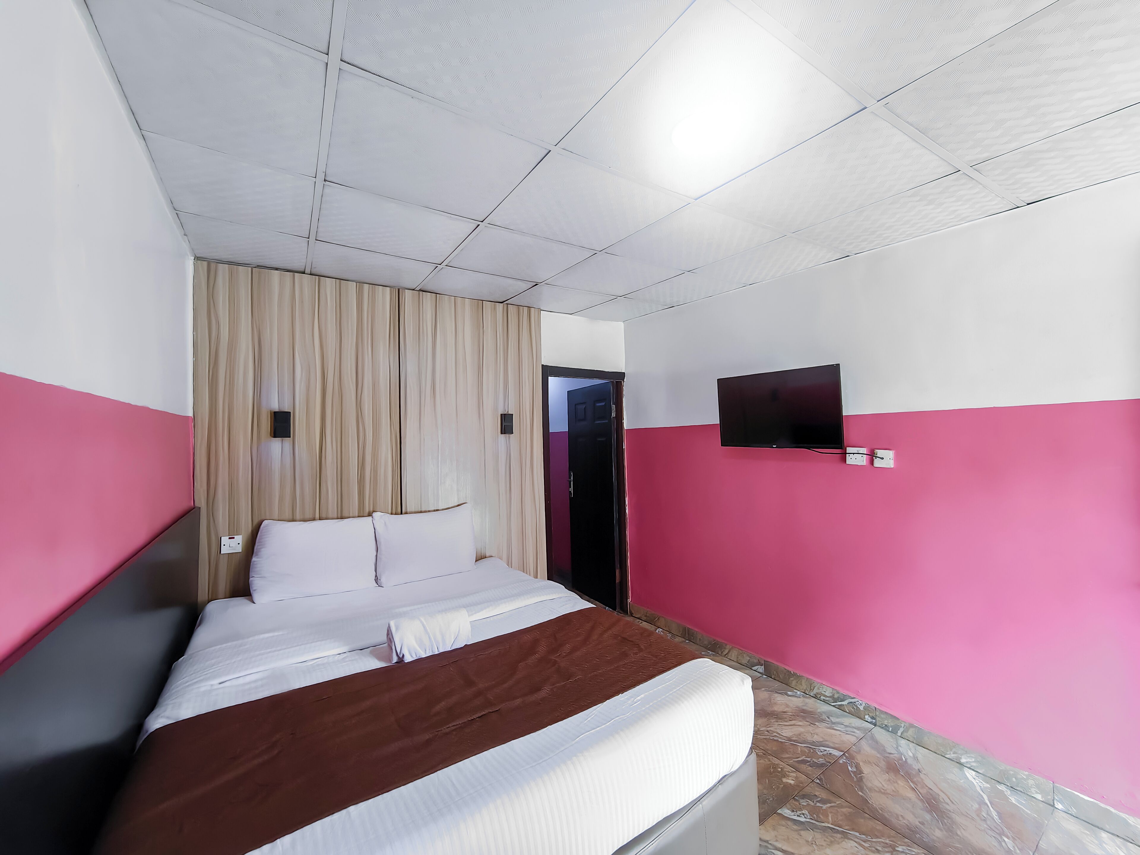 Une chambre d’hôtel avec un lit, un téléviseur fixé au mur et une porte donnant sur une autre pièce.
