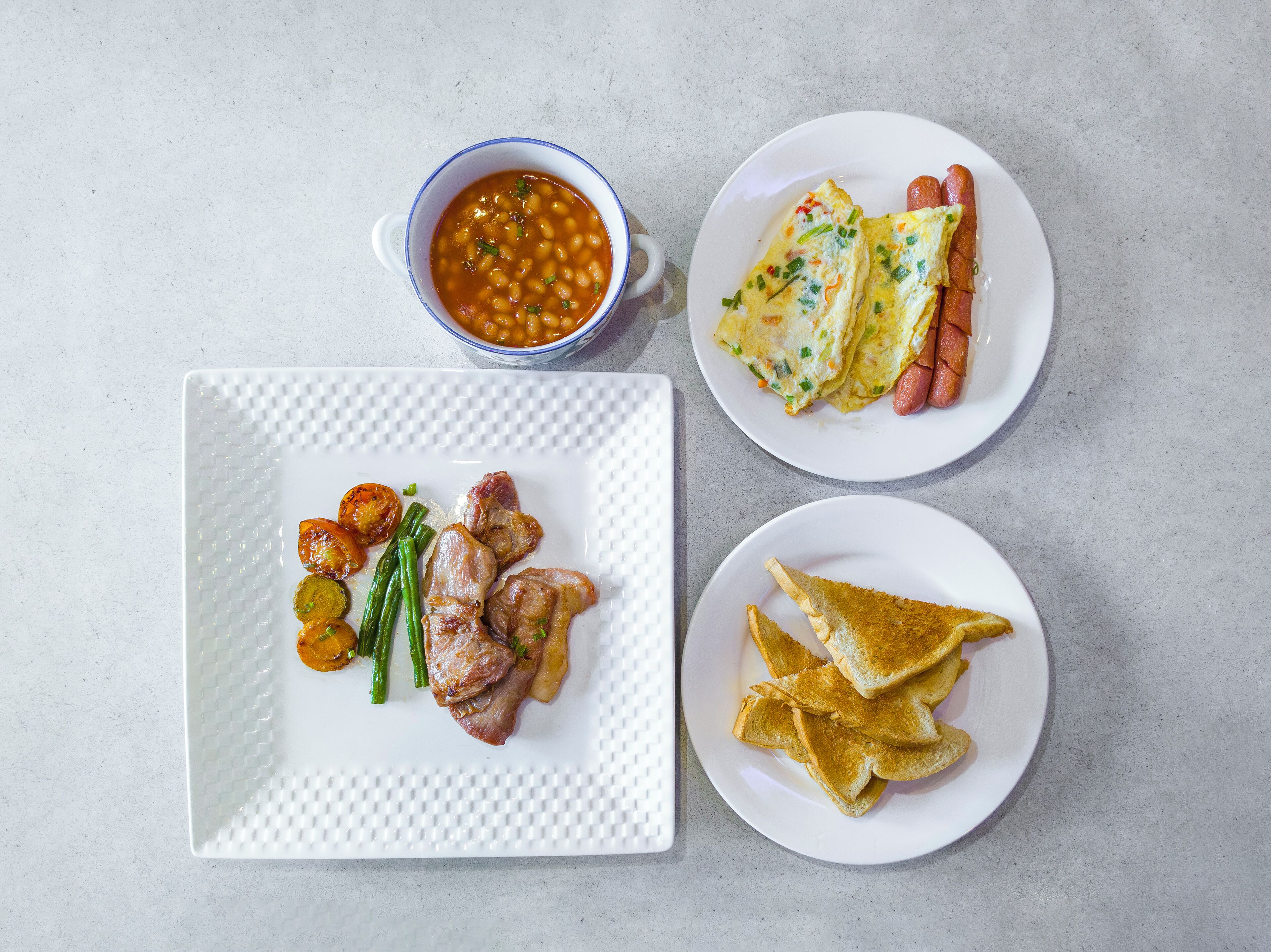 A meal with beans, sausages, omelettes, and toast on plates.