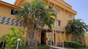 A yellow building with a tiled entrance, palm trees, and a clear sky.
