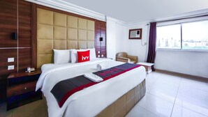 A hotel room with a large bed, a headboard, a bedside table, a chair, a window, and a view of the city.