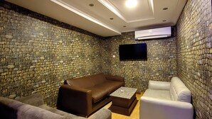 A room with a stone wall, a brown leather sofa, a white armchair, and a flat-screen TV mounted on the wall.