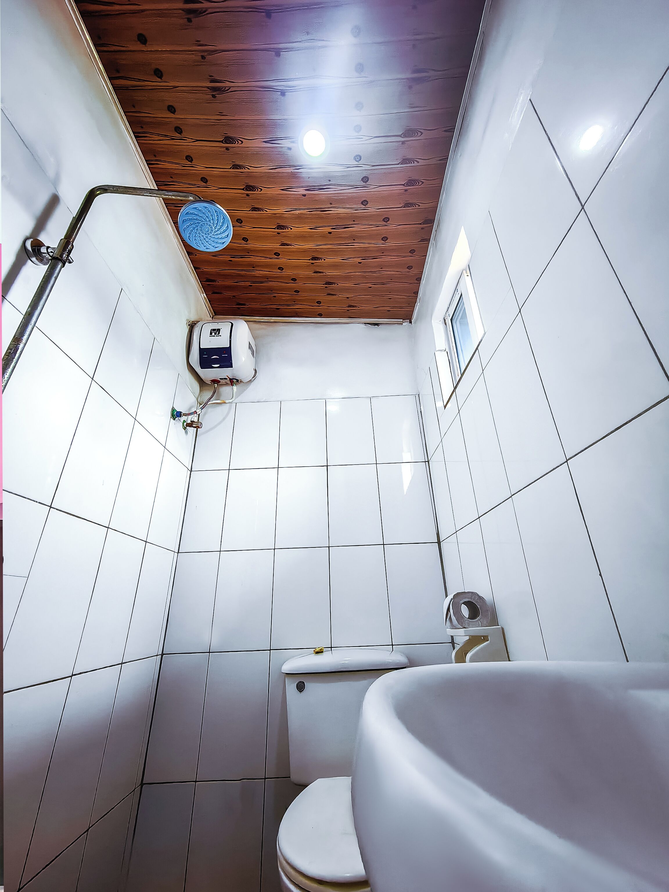 Un baño con paredes de azulejos blancos, techo de madera, inodoro, lavabo y zona de ducha.