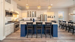 Una cocina moderna con una isla central, electrodomésticos de acero inoxidable, iluminación colgante y un comedor con sillas.