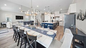 Una cocina moderna con una isla central, comedor con sillas y una escalera que sube a otro nivel.