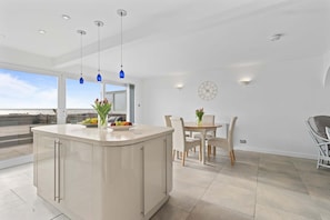 A modern kitchen with a central island, a dining area with a table and chairs, and a large window offering a view.
