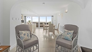 A spacious living area with two grey armchairs, a dining table, and a view of the outdoors through large windows.