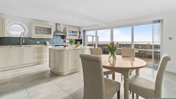A modern kitchen with a central island, dining area with chairs, and a large sliding glass door to a balcony.
