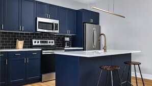 A modern kitchen with dark blue cabinets, stainless steel appliances, and a white countertop. - The Frankford Getaway (Philadelphia)