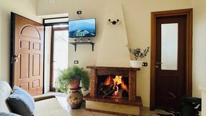 Een woonkamer met een open haard, een aan de muur bevestigde televisie en een deur die naar buiten leidt.