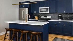 A modern kitchen with dark blue cabinets, stainless steel appliances, and a white island with stools. - Experience Philly in Style (Philadelphia)