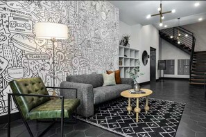 A modern living room with a patterned wall, a grey sofa, a green armchair, a round coffee table, and a staircase in the background. - Art-inspired Philly Getaway (Philadelphia)
