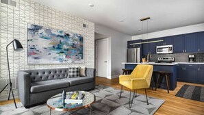 A modern living room with a grey sofa, a yellow armchair, and a coffee table. A large abstract painting adorns the wall, and the room features a geometric patterned rug. - Art-inspired Philly Getaway (Philadelphia)