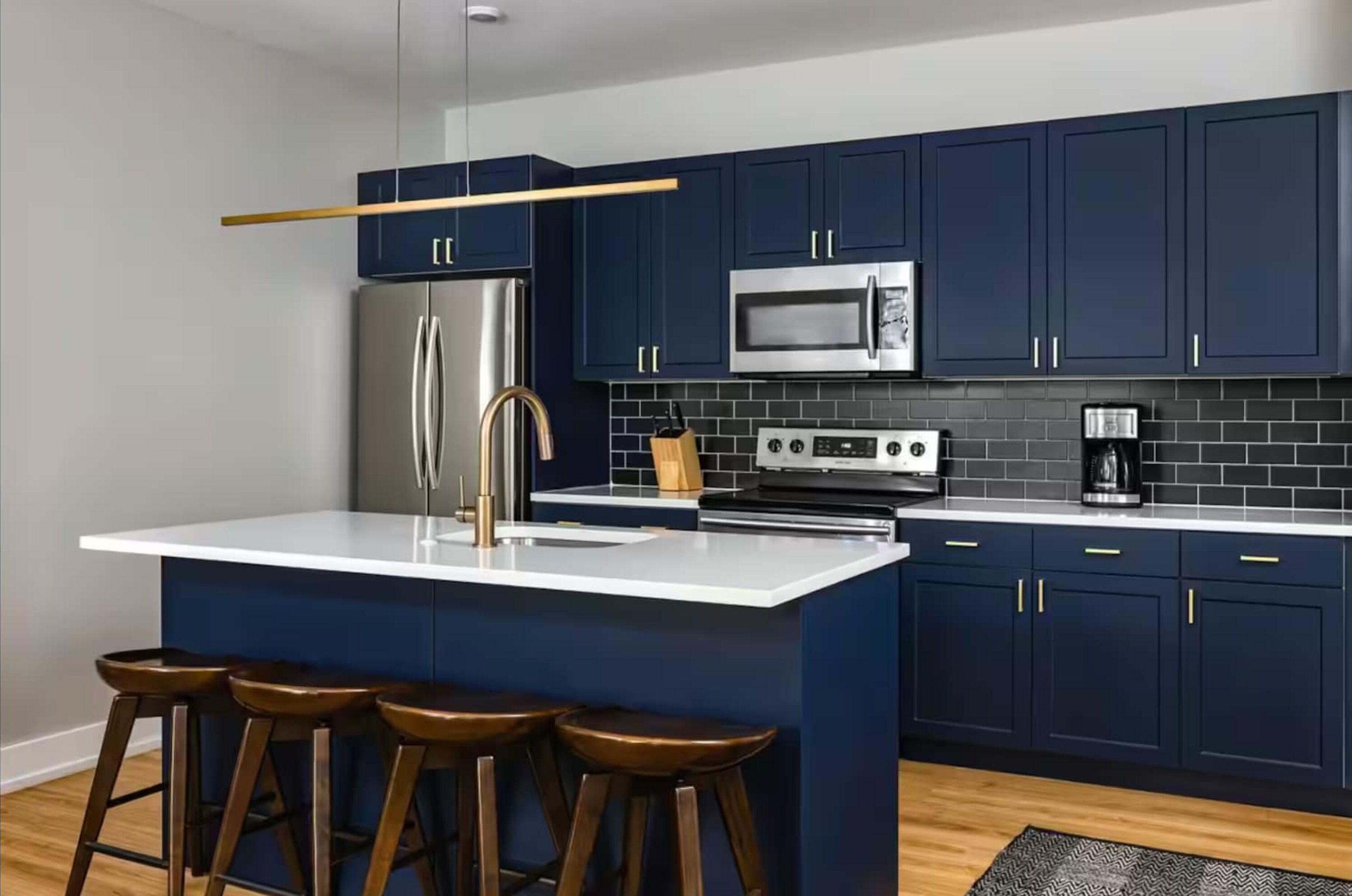 A modern kitchen with dark blue cabinets, stainless steel appliances, and a white island with stools.