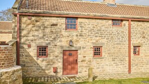 Un bâtiment en pierre avec un toit recouvert de tuiles, une porte centrale et de petites fenêtres.