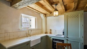 Une cuisine avec une fenêtre, des poutres apparentes en bois au plafond, un évier, des placards et une table à manger.