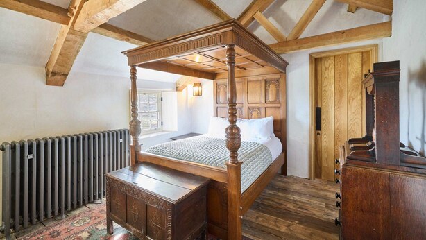 Un lit traditionnel à baldaquin, doté d’une tête de lit en bois, d’une commode en bois et d’un radiateur posé sur le sol.