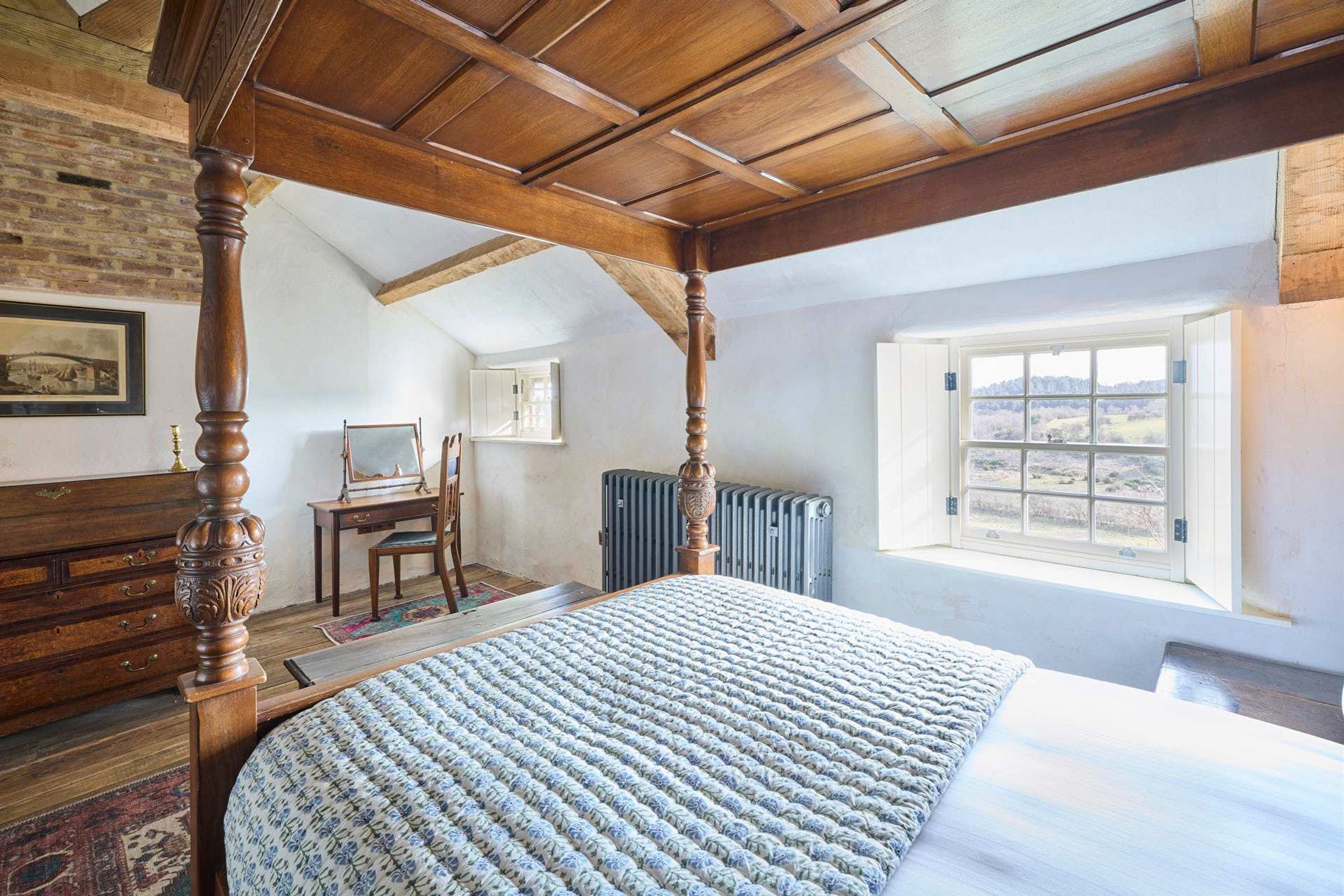 Una camera da letto con un letto a baldacchino, soffitto in legno, termosifone, scrivania e finestra con vista.