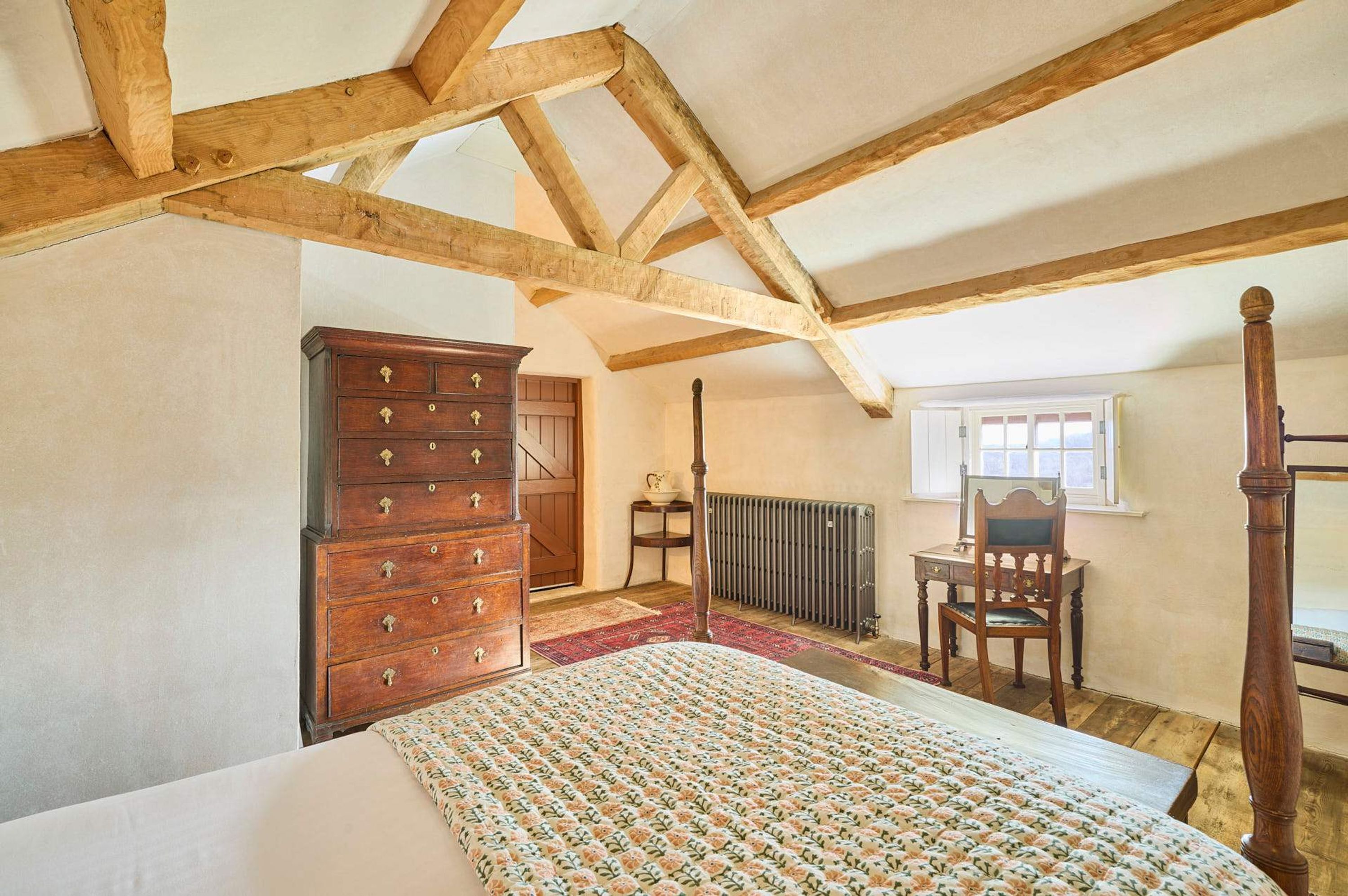 A bedroom with a four-poster bed, wooden dresser, and a radiator.