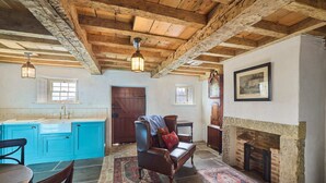 Ein rustikales Interieur mit freiliegenden Holzbalken, einem Kamin aus Stein, einer blauen Küche und einem traditionellen Ledersofa.